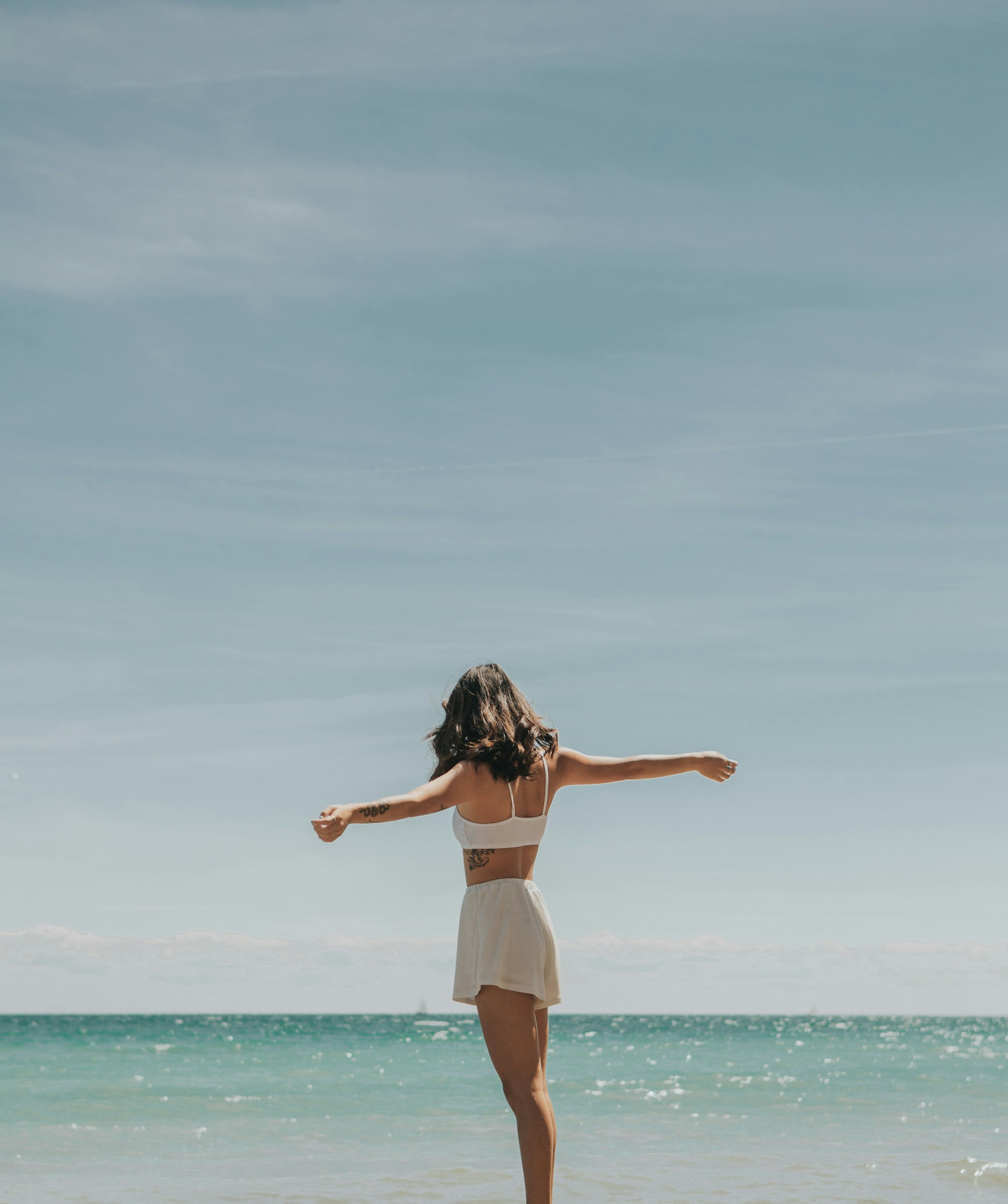 Woman standing at the shoreline with arms out, facing the ocean